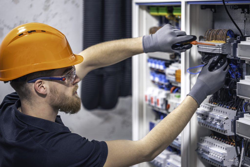 A male electrician works in a switchboard with an electrical connecting cable.